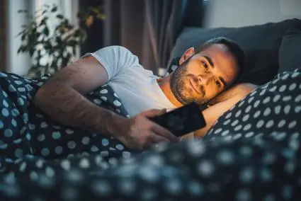 Homme souriant, envoyer des SMS au lit